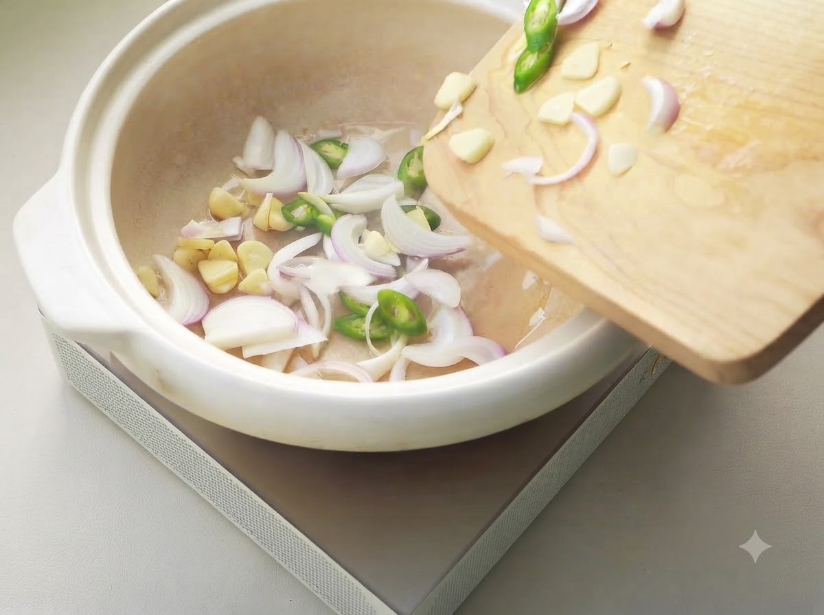Cipolle a fette, aglio e peperoncini sfrigolanti in una pentola di ceramica bianca.