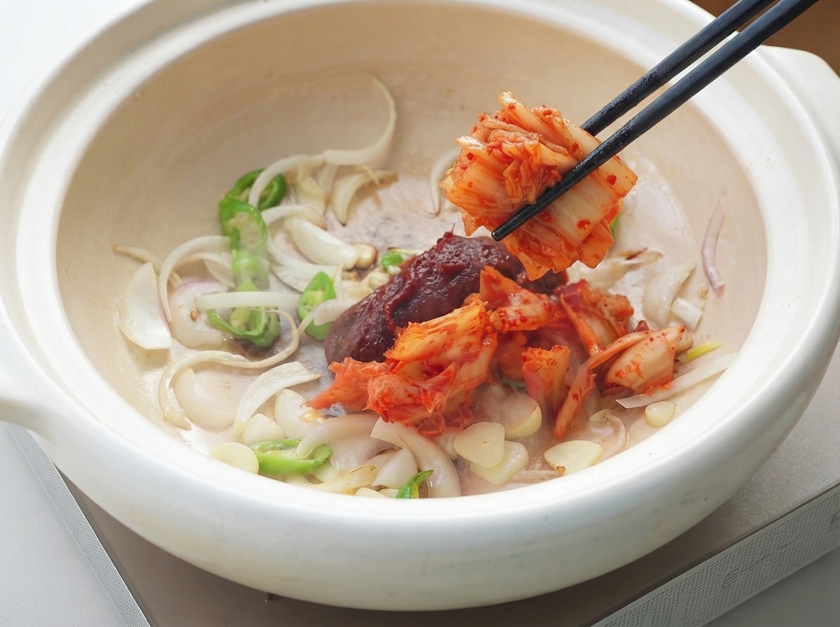 Pasta di peperoncino coreana e kimchi aggiunti alla pentola con gli aromi usando delle bacchette.