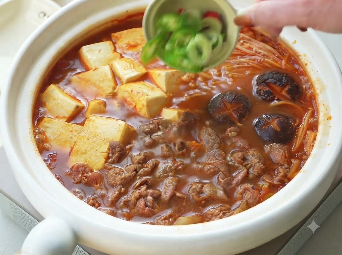 Cipollotti e peperoncini affettati versati da una ciotolina come guarnizione sopra lo stufato coreano di manzo e tofu.