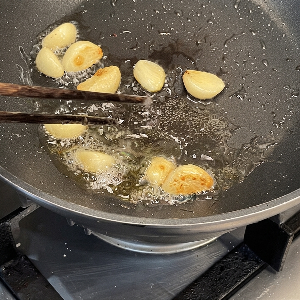 Spicchi daglio saltati nellolio in una padella calda usando le bacchette.