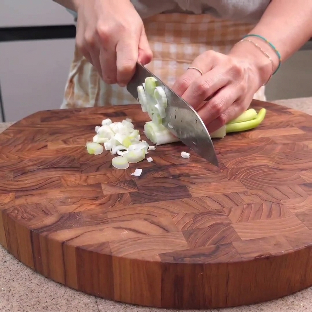 Cipollotti tagliati su un tagliere di legno con un coltello da cucina.