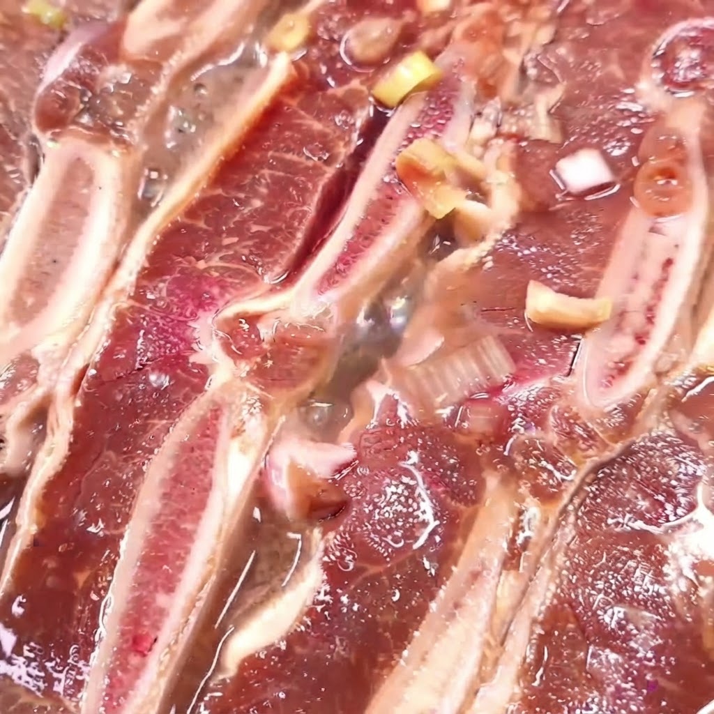 Costine di manzo che cuociono in una padella con marinata che si riduce e fa le bolle.