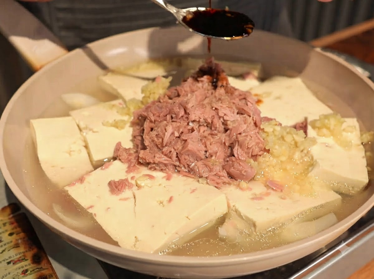 Salsa di soia scura fatta gocciolare da un cucchiaio al centro dei pezzi di tonno e tofu.