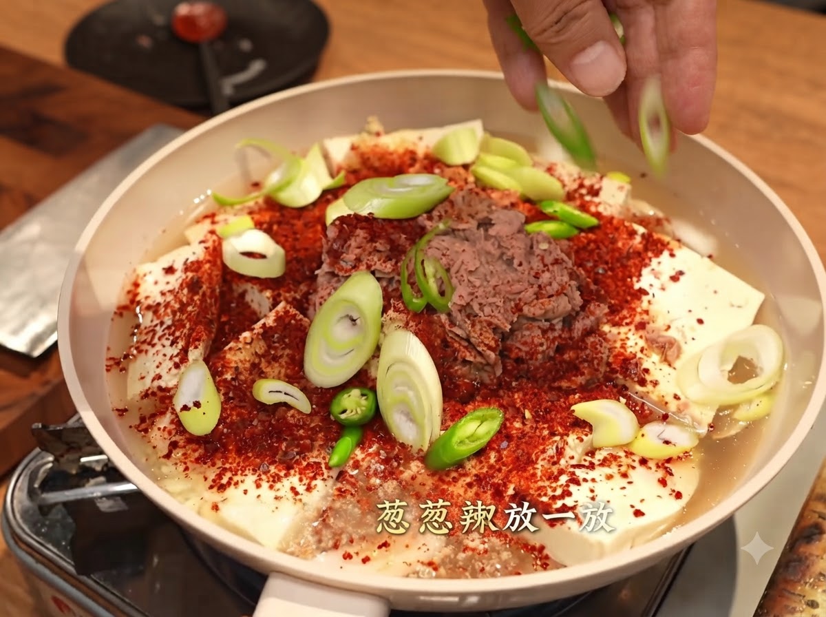 Mani che cospargono cipollotti affettati e peperoncini verdi su una padella coperta di fiocchi di peperoncino rosso, tofu e tonno.