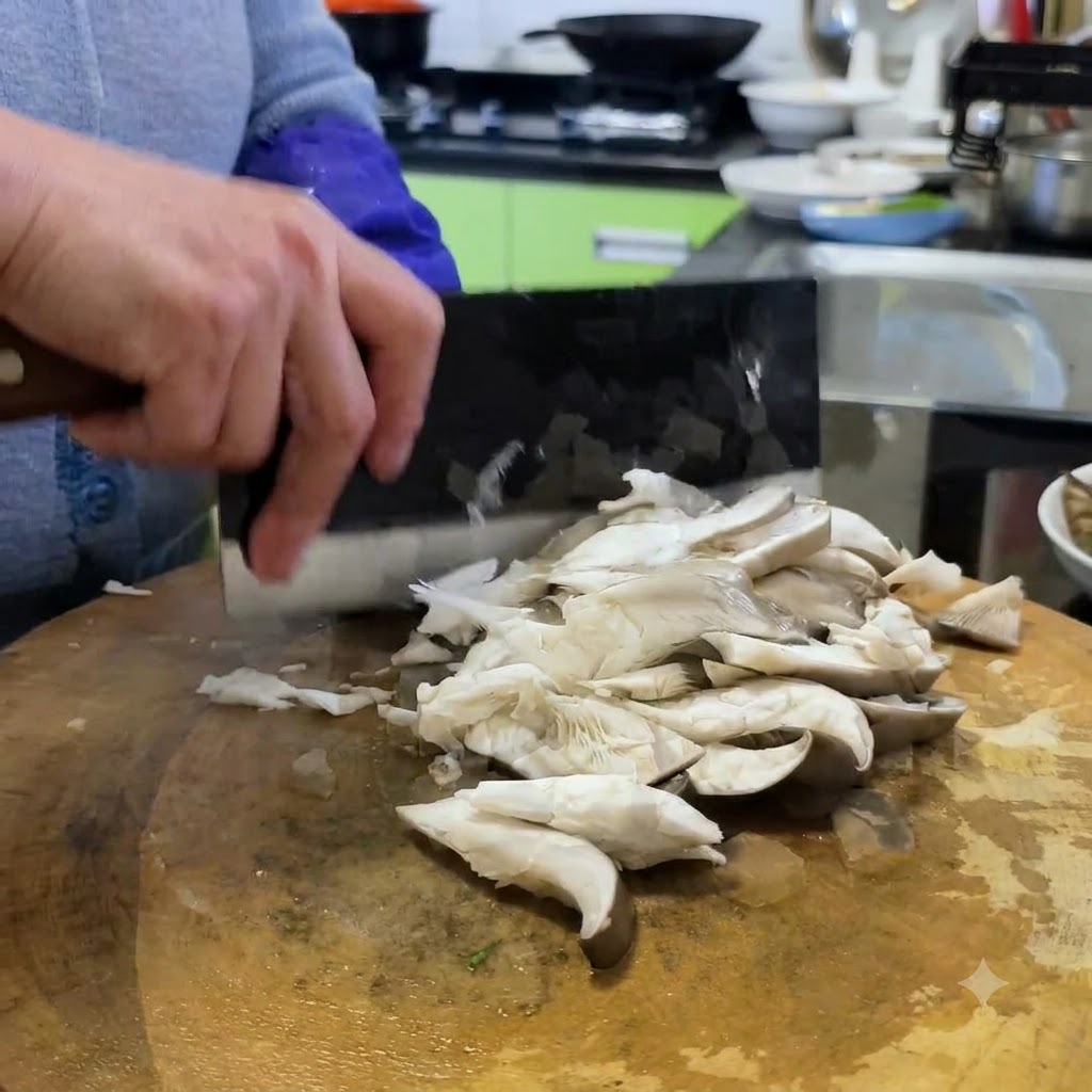 Funghi orecchioni tagliati a porzioni più piccole su un tagliere di legno usando una mannaia.