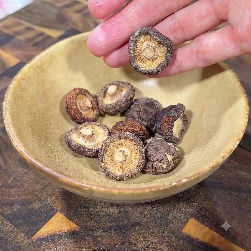 Funghi shiitake secchi adagiati allinterno di una ciotola di ceramica gialla su una superficie di legno.