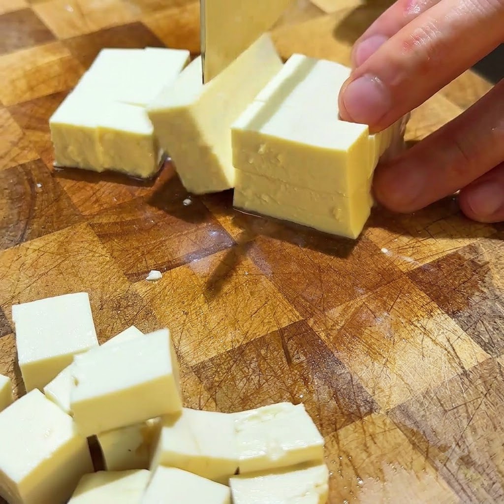 Tofu vellutato tagliato in piccoli cubetti ordinati su una superficie di taglio di legno.