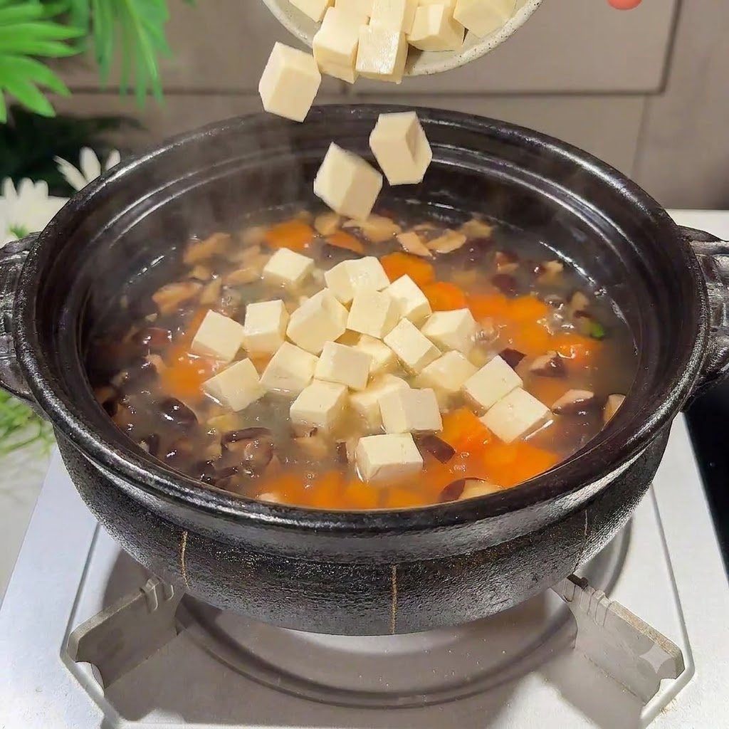 Pezzi di tofu vellutato a cubetti che cadono nella pentola della zuppa in ebollizione.