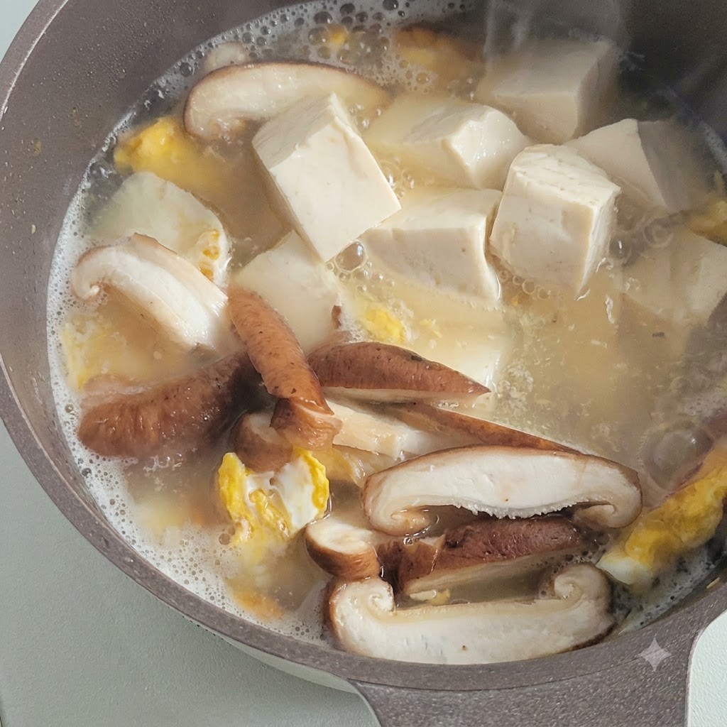 Cubetti di tofu bianco morbido che sobbollono in un brodo saporito insieme a funghi affettati e pezzi di uovo fritto.