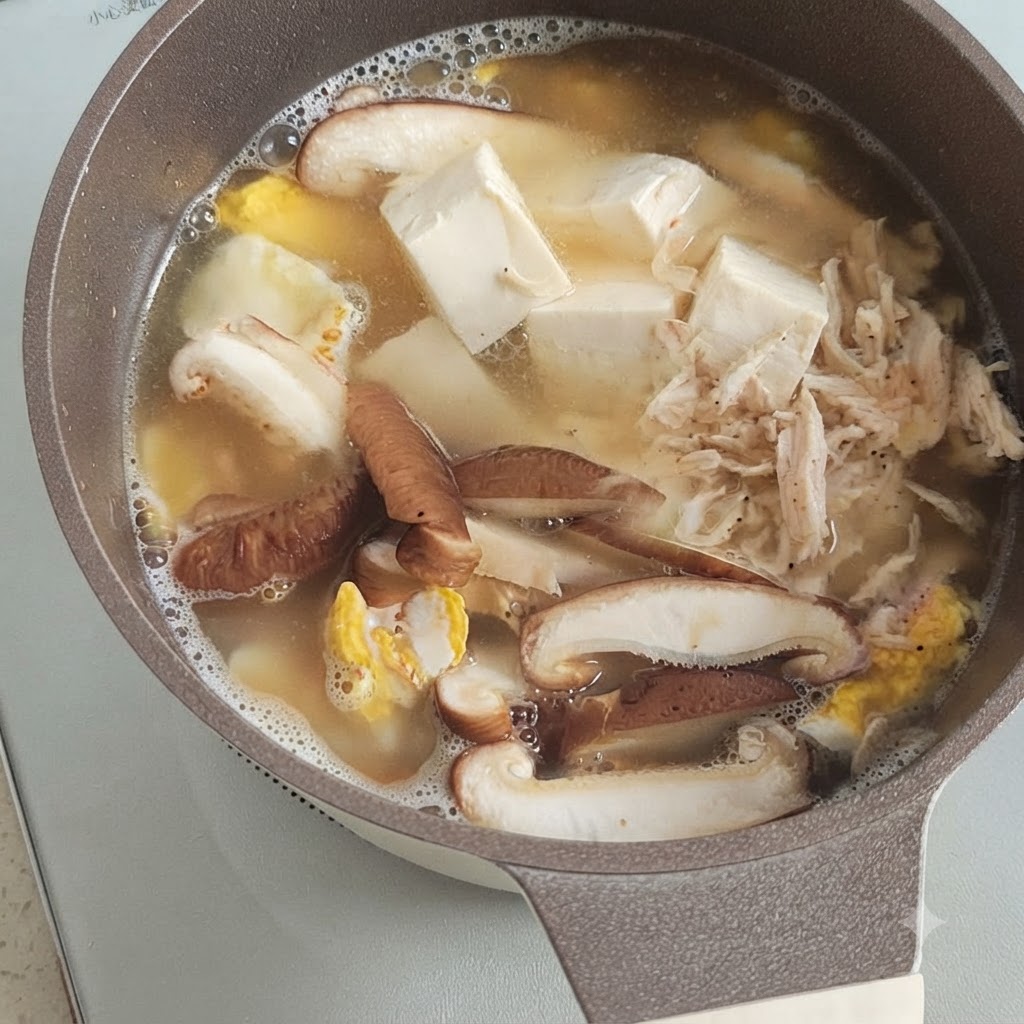 Un piccolo mucchietto di gamberetti secchi sopra tofu, funghi e uovo che sobbollono in una pentola di brodo.