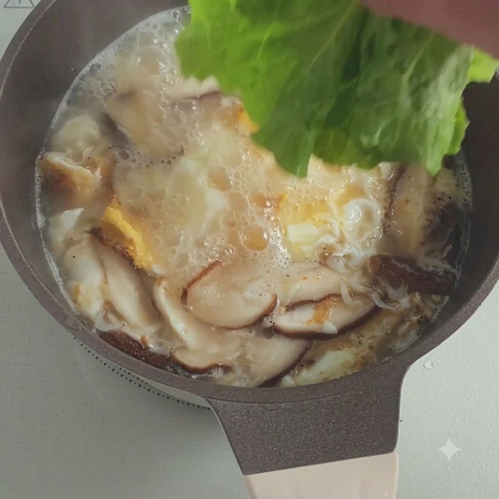 Foglie di lattuga fresca che vengono messe in una pentola di zuppa bollente con funghi e uova.