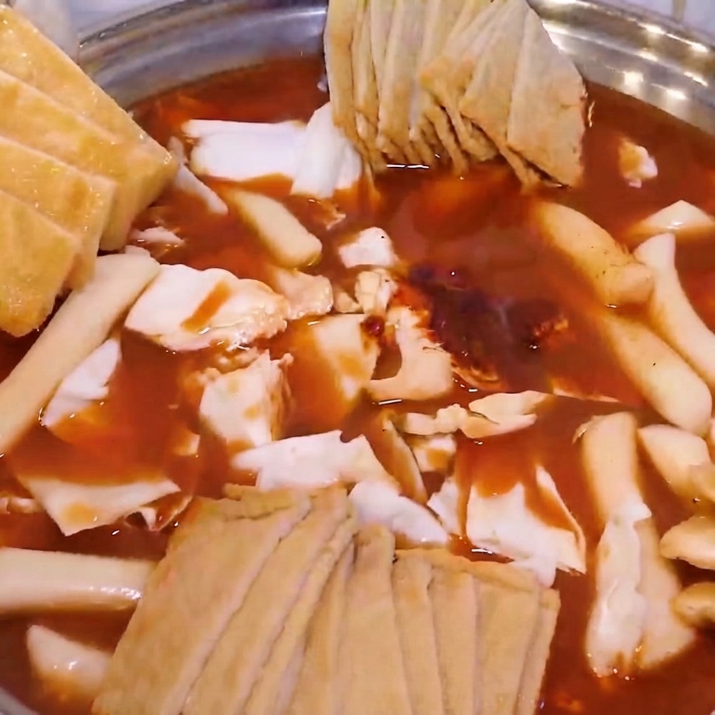 Un hot pot assemblato pieno di cavolo, gnocchi di riso, torte di pesce e guarnito con tofu fritto e cipollotti.