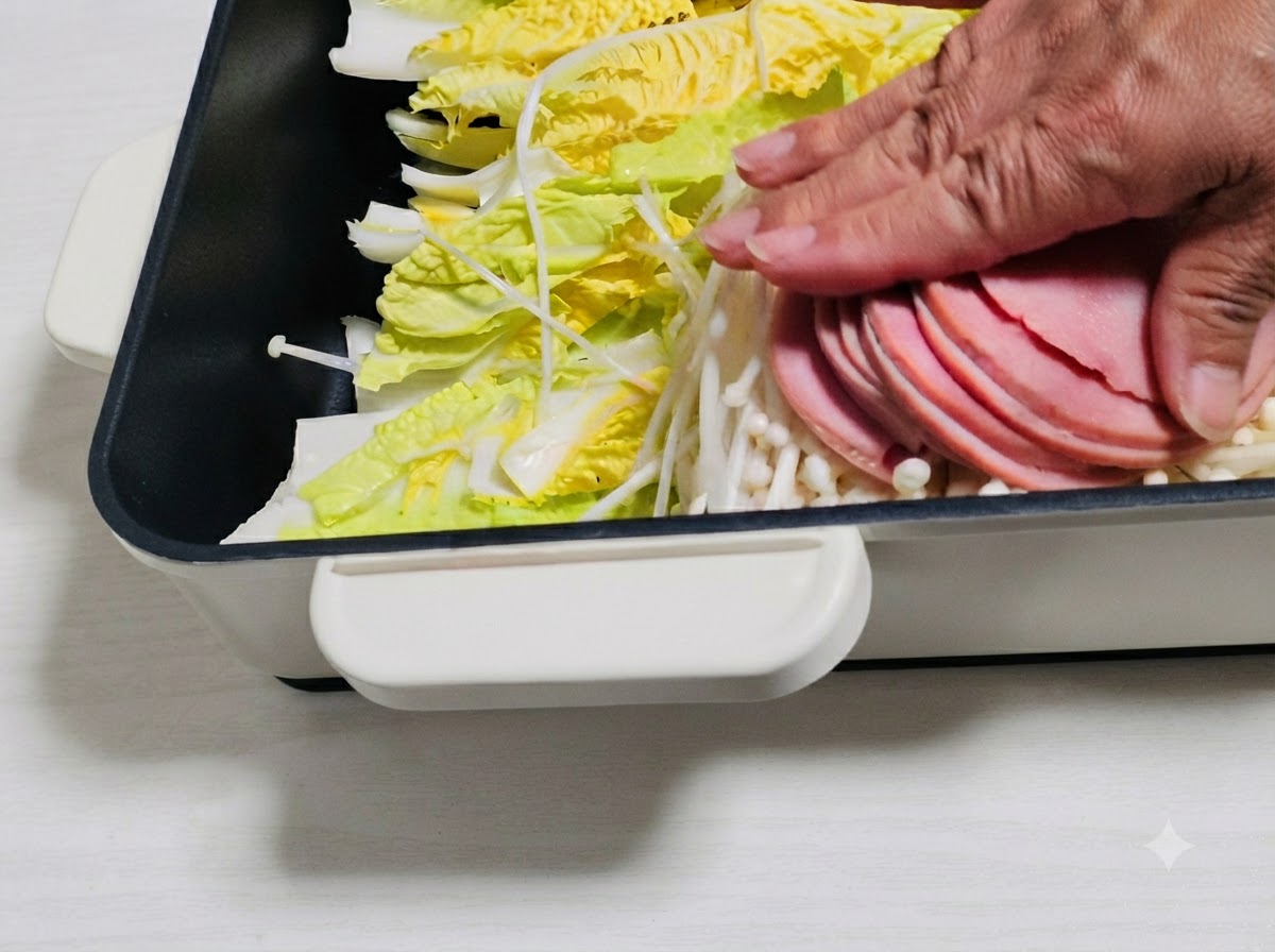 Fette di prosciutto e altri ingredienti disposti sopra le verdure nella pentola.