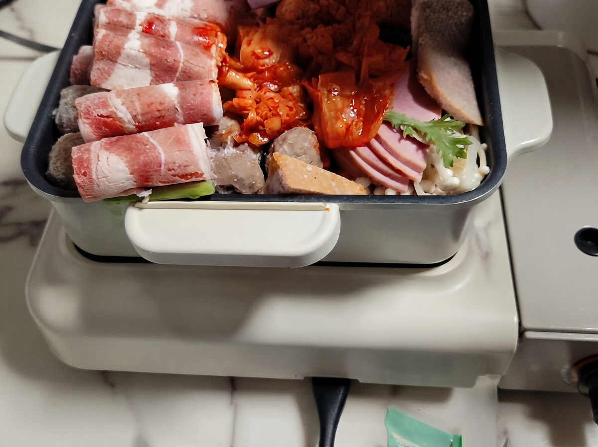 Un hot pot riempito con strati disposti di carne, verdure e torte di riso con il brodo versato sopra.
