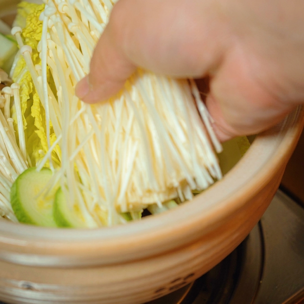 Funghi enoki freschi posizionati sopra le verdure nella pentola.