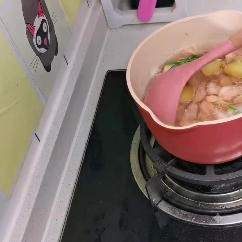 Piccoli gamberi bianchi mescolati in una pentola di stufato di ramen in stile coreano che sobbolle usando una spatola rosa.
