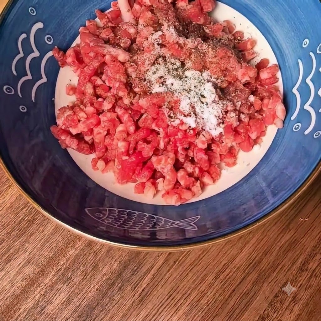 Carne macinata di manzo e maiale in una ciotola decorata in blu con sale e pepe nero spolverati sopra.
