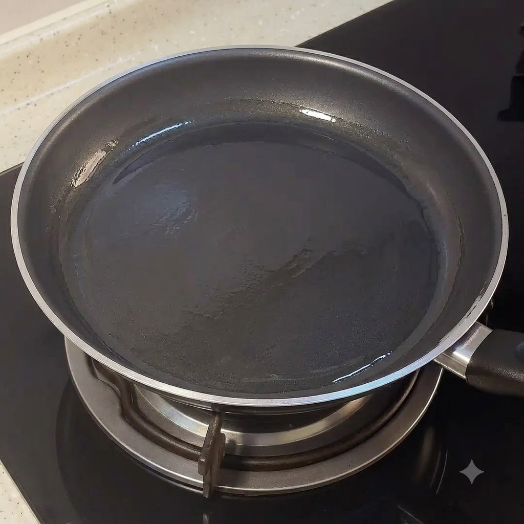 Una padella nera vuota posizionata su un fuoco del piano cottura con un velo leggero dolio.