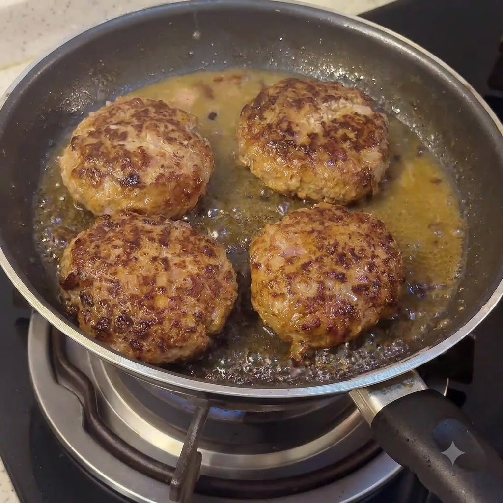 Un panetto di burro e componenti della salsa che si sciolgono nella padella insieme agli hamburger che sfrigolano.