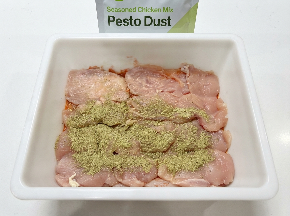 Polvere di pepe rattan verde generosamente spolverizzata sulle cotolette di pollo crudo allinterno di un contenitore bianco.