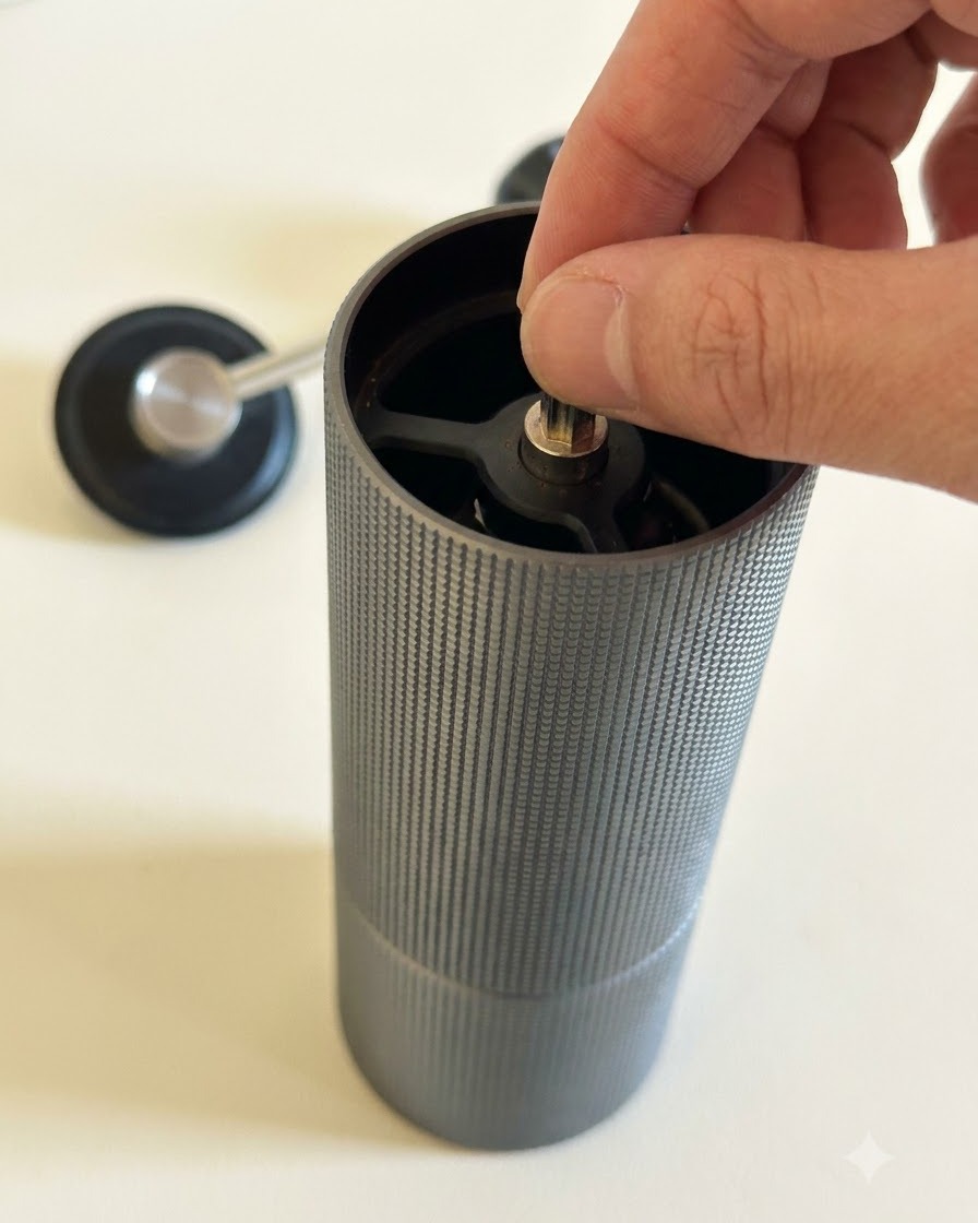 Chicchi di caffè macinati allinterno di un macinino manuale con una maniglia di metallo vicina.