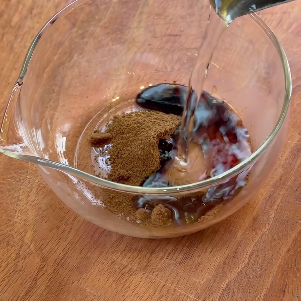 Acqua versata da una piccola brocca in una ciotola di vetro contenente caffè liquido e condimenti.