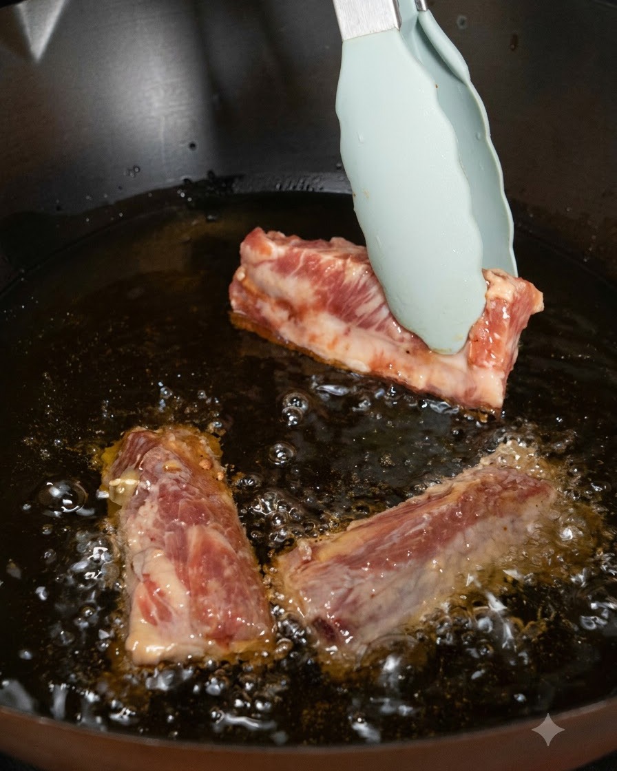 Pezzi di costine di maiale inseriti con le pinze nellolio caldo allinterno di un wok.