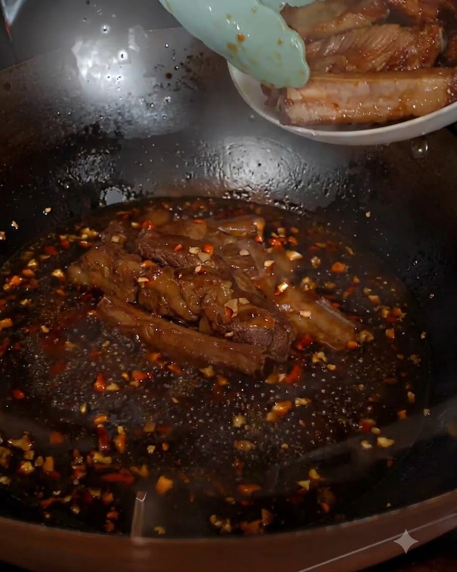 Costine di maiale fritte inserite con le pinze nella salsa bollente nel wok.