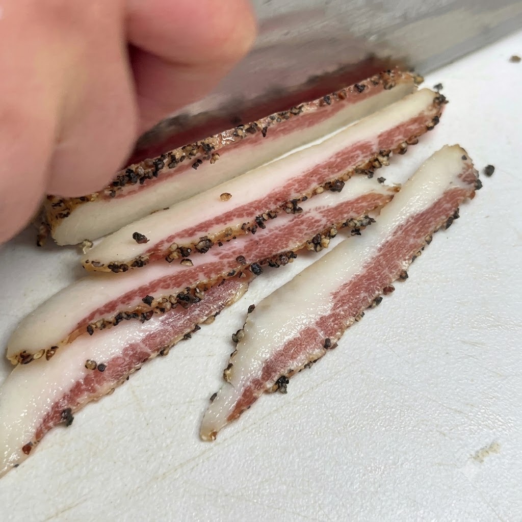 Guanciale di maiale italiano stagionato ricoperto di pepe nero mentre viene affettato su un tagliere.