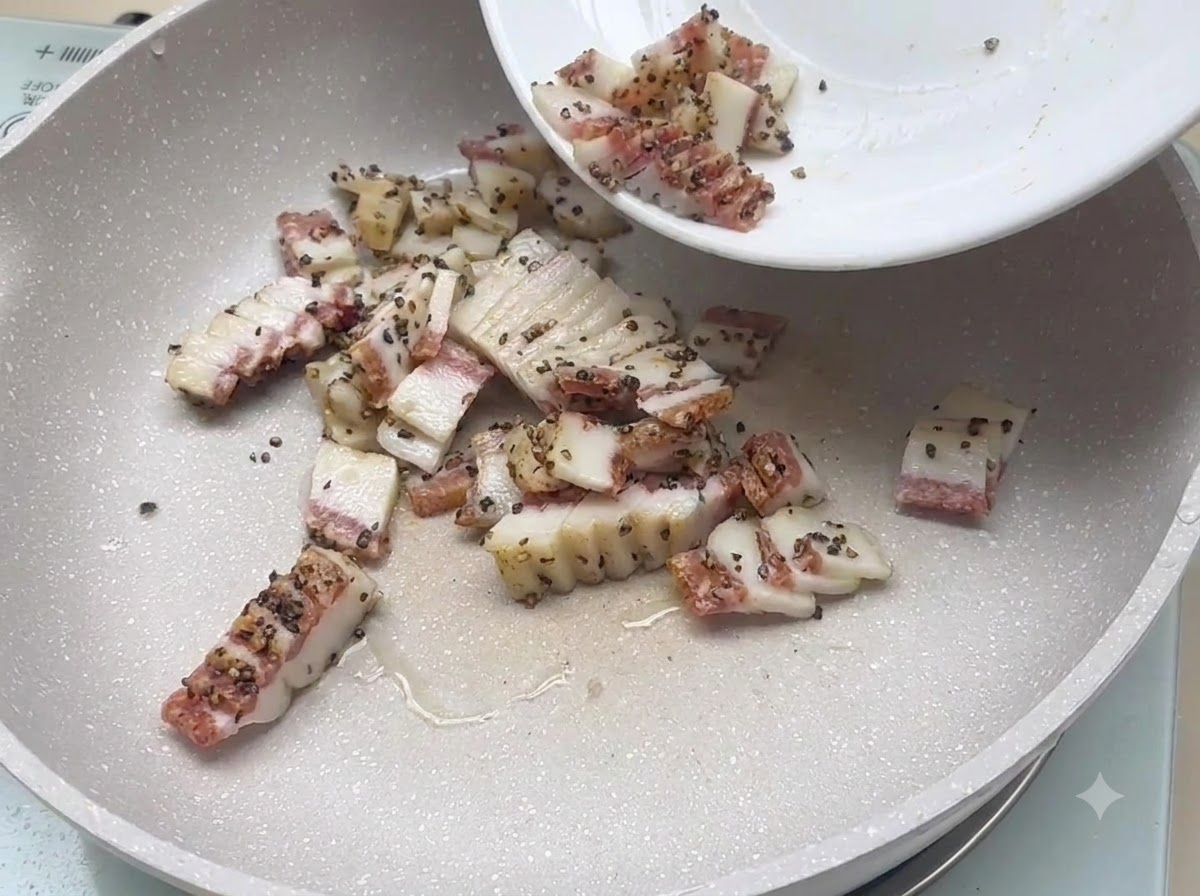 Pezzi cubettati di guanciale stagionato aggiunti da un piatto in una padella piatta per la frittura.