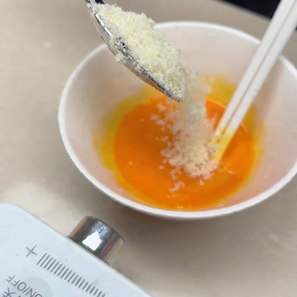 Formaggio Parmigiano grattugiato mescolato a tuorli duovo di colore arancione vivo in una ciotolina con bacchette bianche.