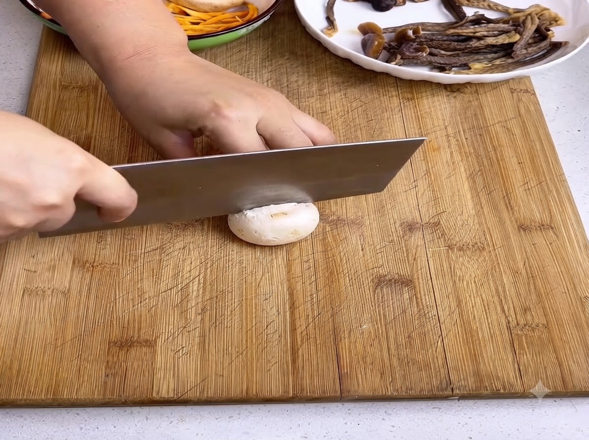 Un coltello da cucina che affetta un fungo champignon bianco su un tagliere di legno.