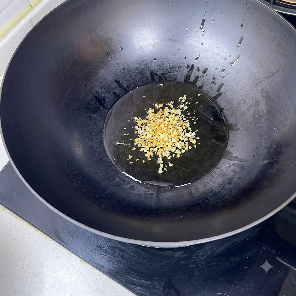 Aglio tritato che frigge in olio bollente allinterno di un wok nero.