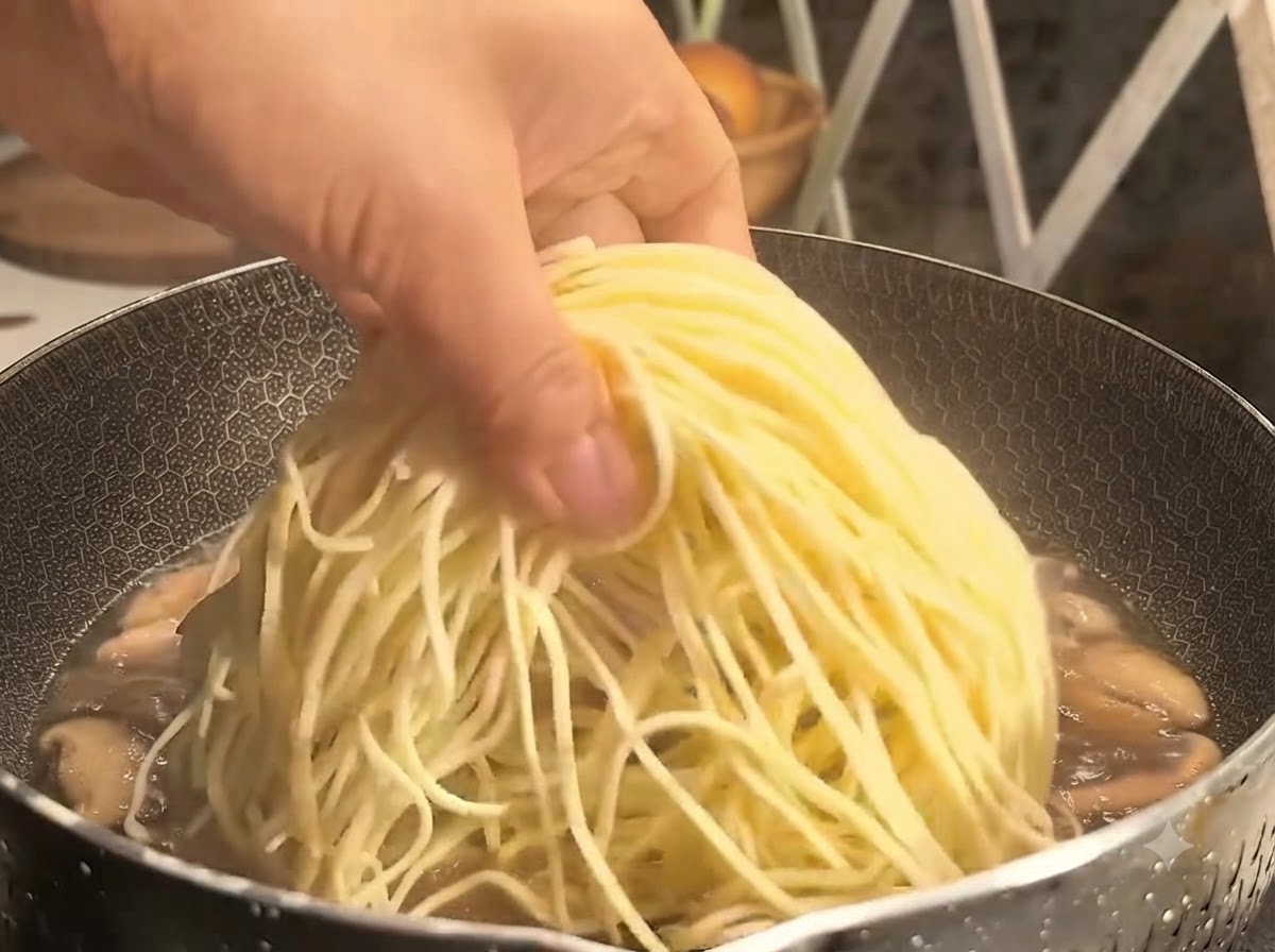 Una mano che posiziona un mazzetto di noodles gialli sottili in una pentola bollente di brodo di funghi.