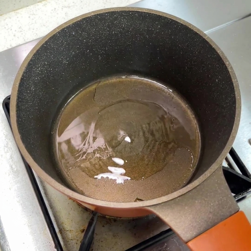 Una piccola pentola da cucina sul fuoco contenente olio caldo.
