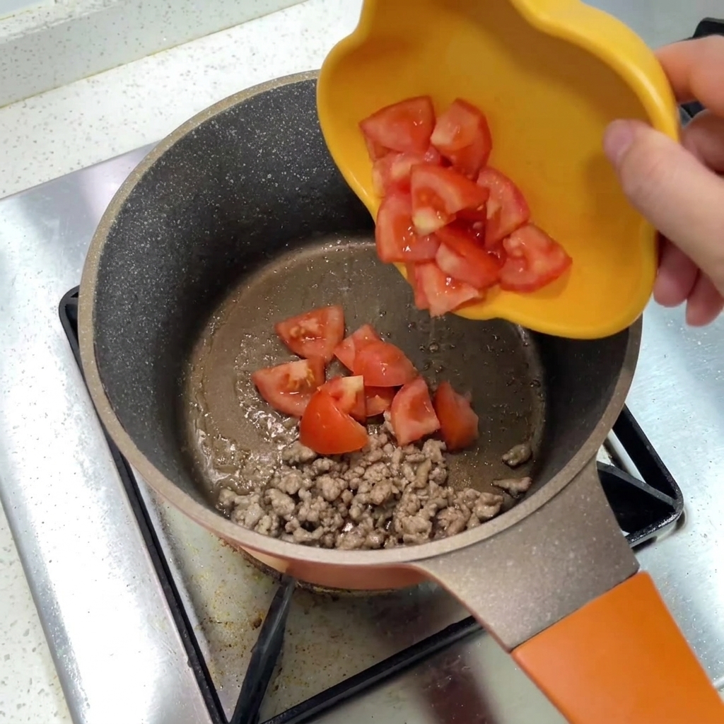 Pomodori a pezzi che scivolano da un piatto giallo in una pentola con carne macinata.