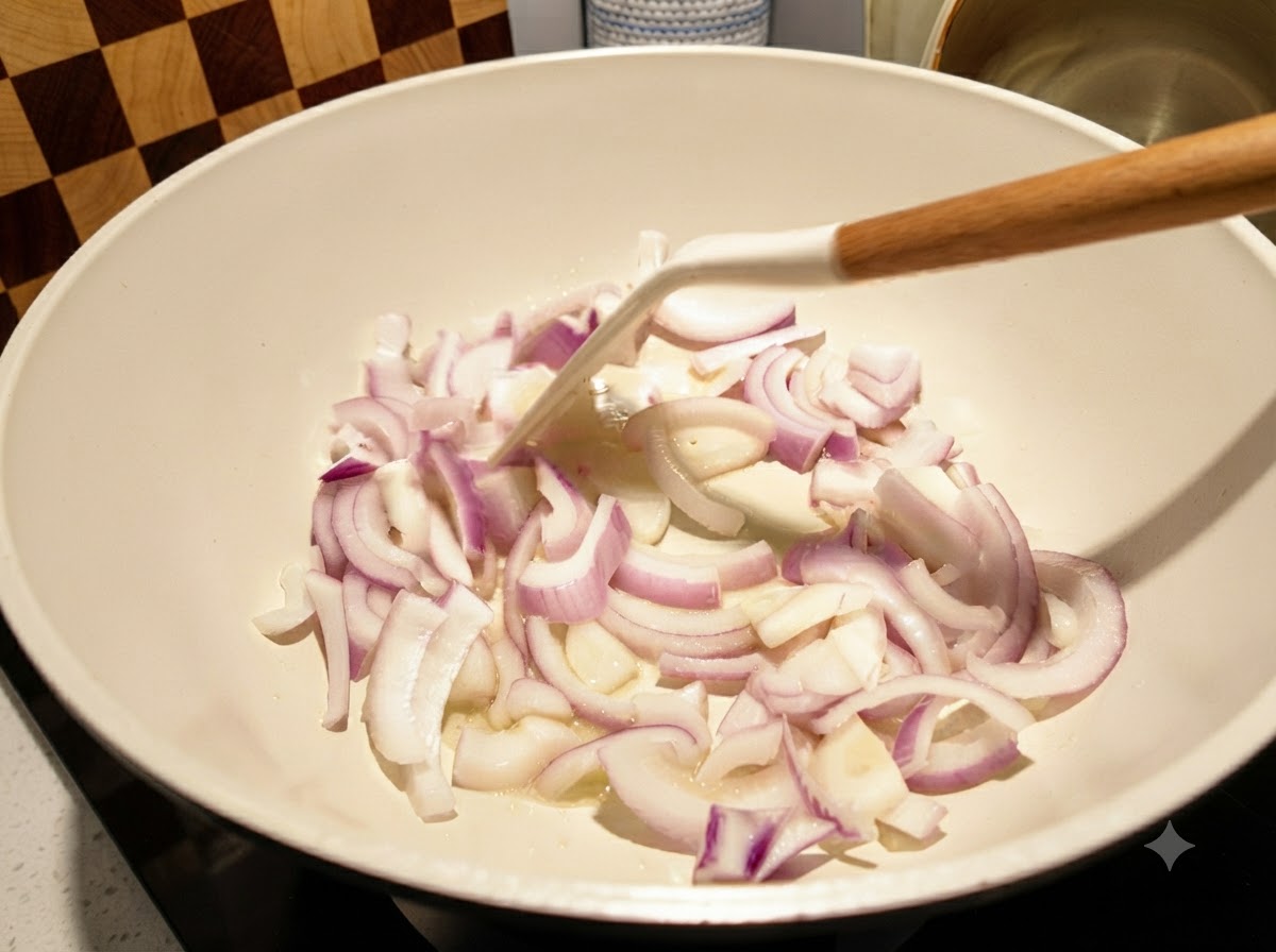 Cipolle rosse affettate saltate in padella bianca con una spatola bianca.
