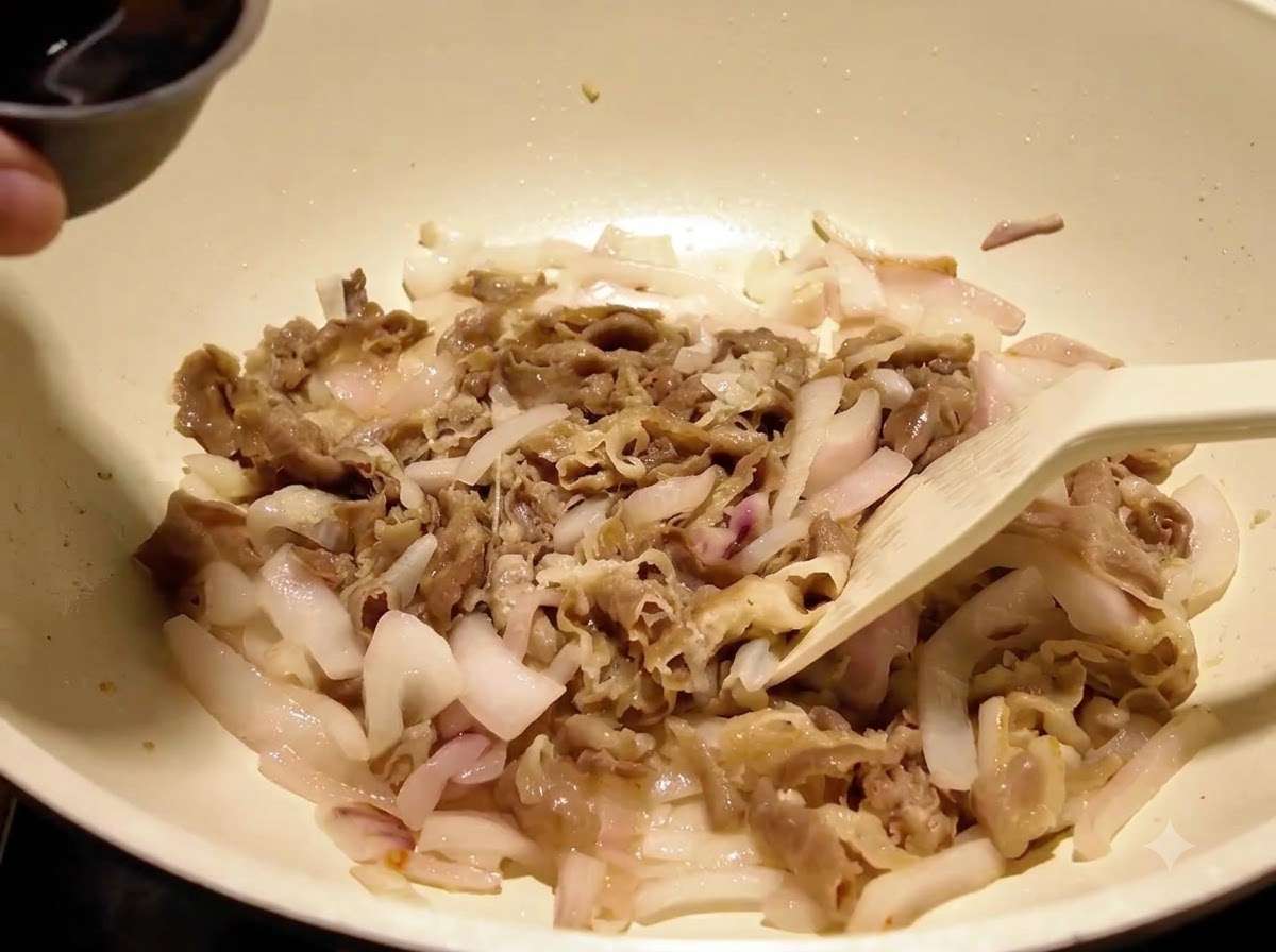 Salsa liquida scura versata da una ciotolina di metallo sul manzo e sulle cipolle in una padella.