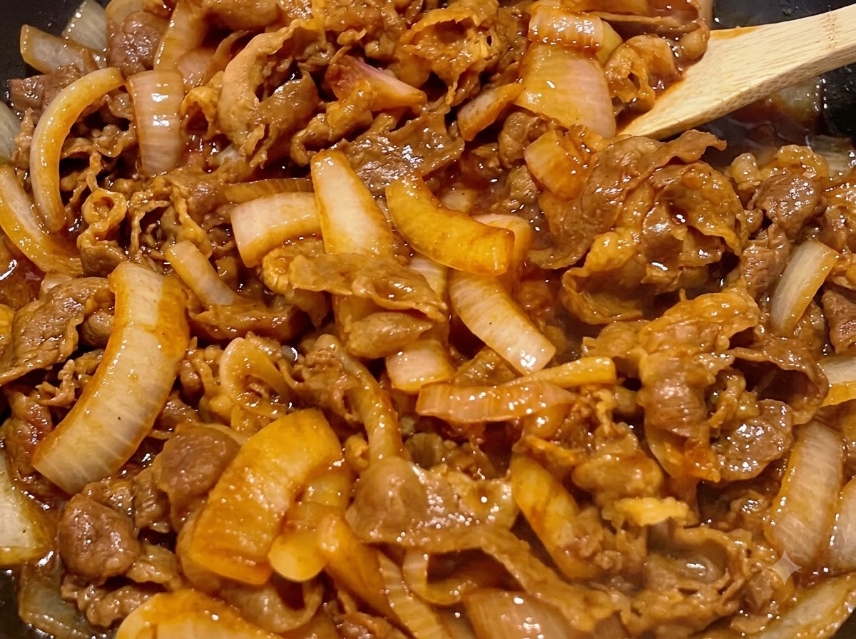 Manzo e cipolle mescolati con una spatola di legno mentre sobbollono in una salsa densa color marrone scuro.