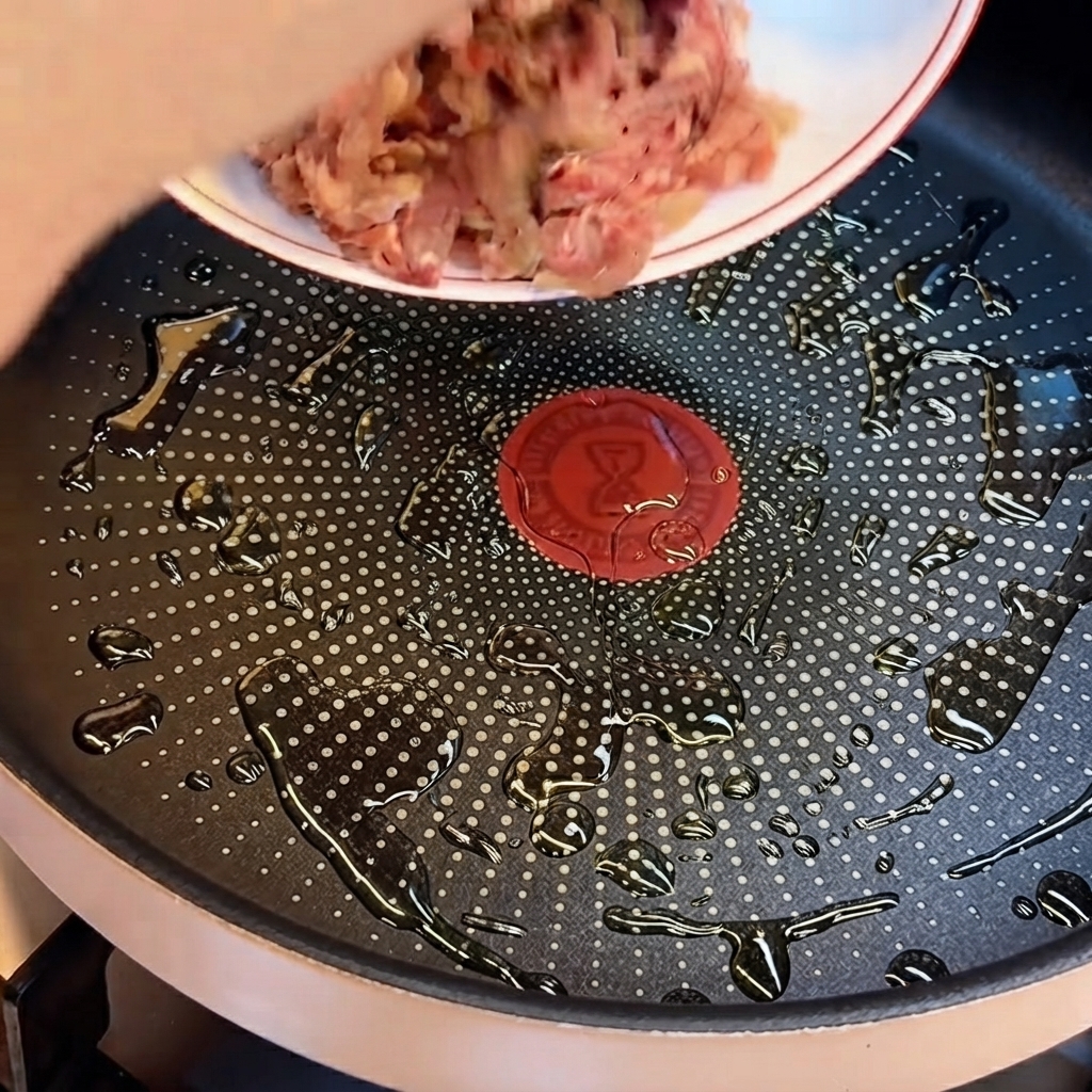 Carne bovina macinata cruda che viene fatta cadere da un piatto in una padella con pozzanghere di olio da cucina.