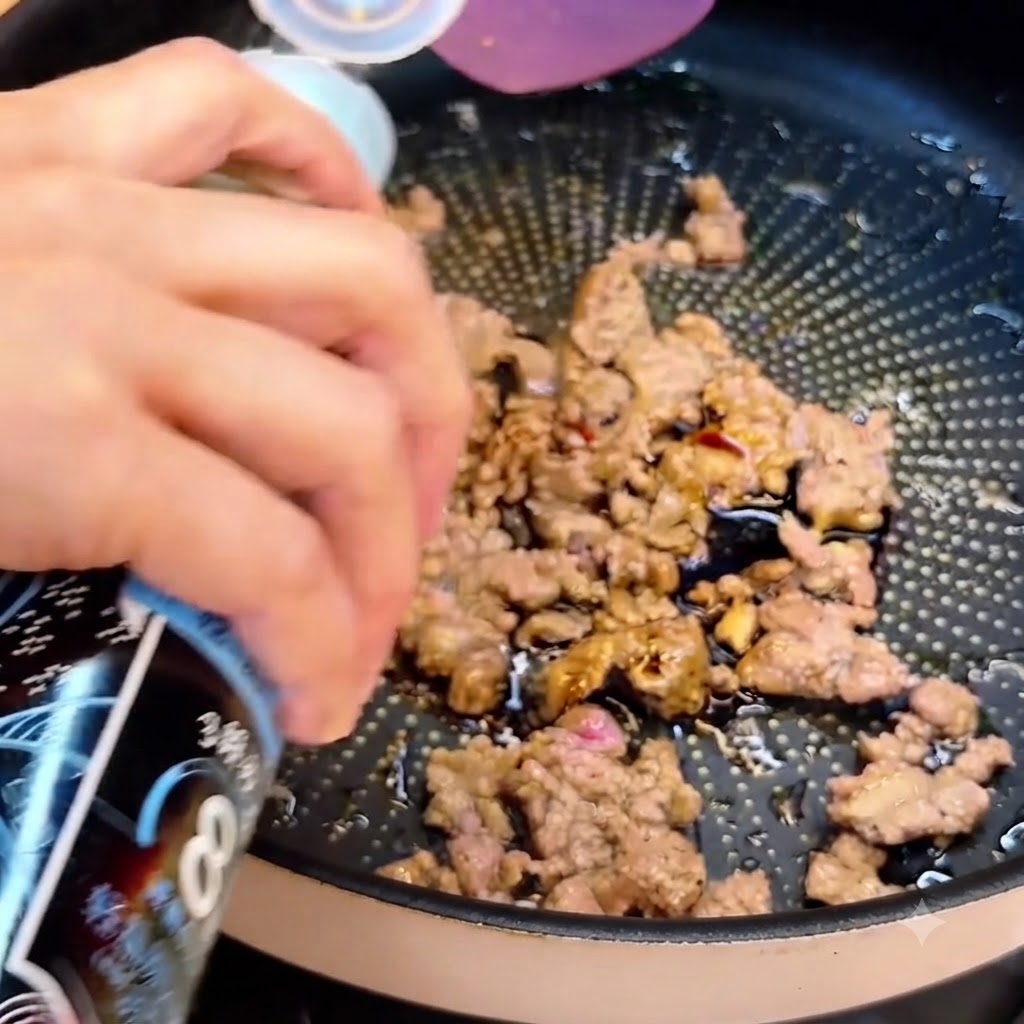 Una bottiglia che eroga salsa di soia sopra la carne macinata rosolata nella padella.