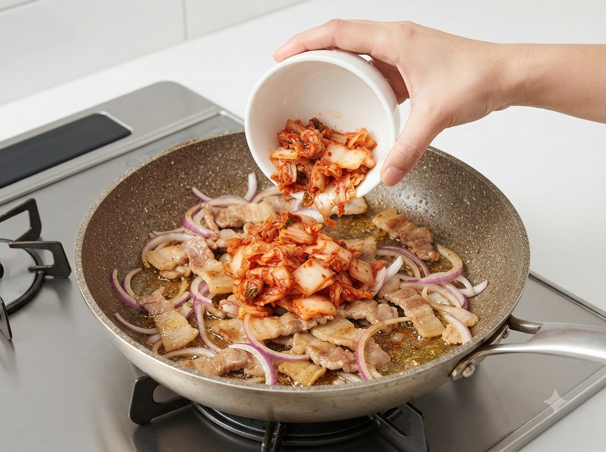 Una ciotola di kimchi tritato versata nella padella rovente con maiale e cipolle.