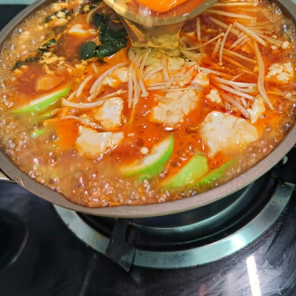 Un uovo rotto in una pentola di zuppa di tofu piccante coreana in ebollizione, piena di funghi e verdure.