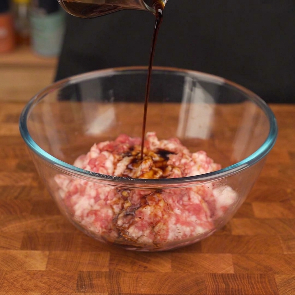 Carne di maiale macinata in una ciotola di vetro mescolata con pepe nero e salsa da mani con guanti.
