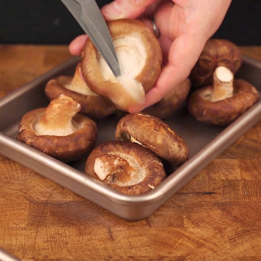Forbici che tagliano il gambo di un fungo shiitake fresco allinterno di una teglia di metallo.