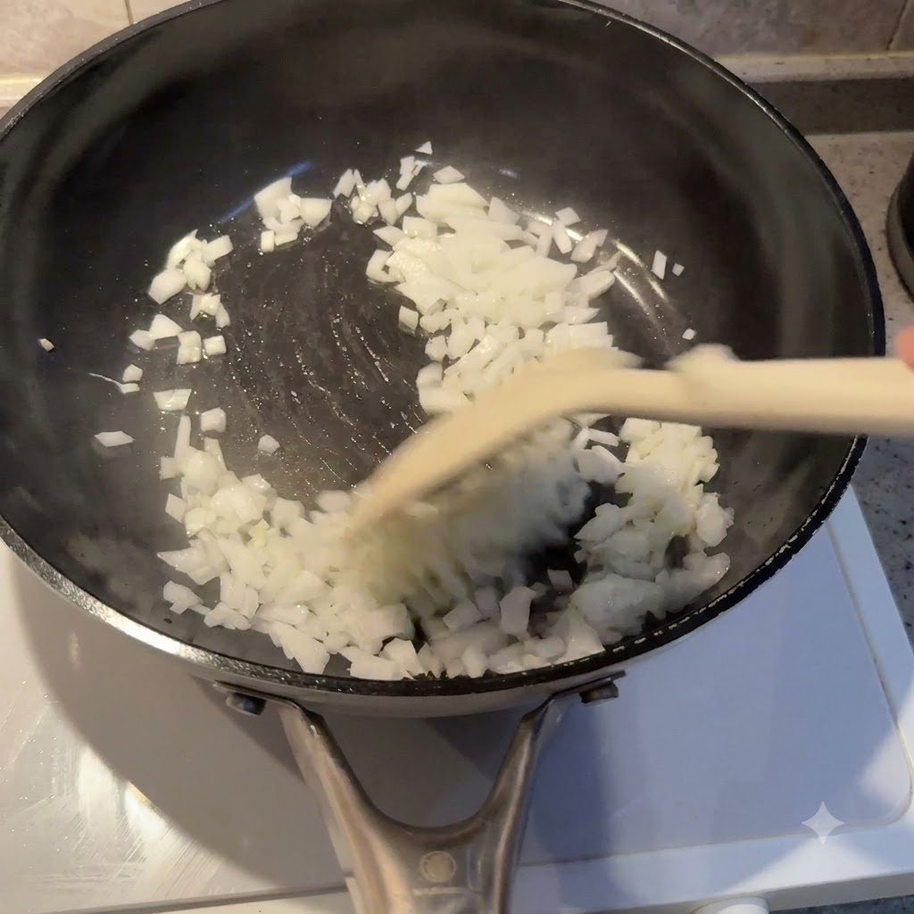 Cipolle a dadini saltate e cotte nellolio allinterno di una padella nera con una spatola.