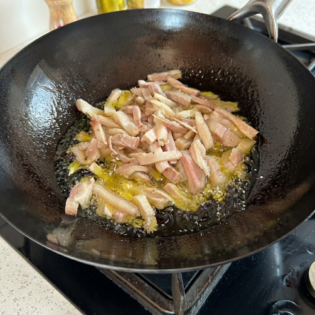 Straccetti di maiale che sfrigolano nellolio bollente allinterno di un wok nero.