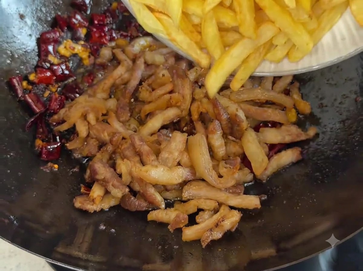Un piatto che fa scivolare i bastoncini di patate dorate in un wok pieno di maiale fritto e spezie al peperoncino rosso scuro.