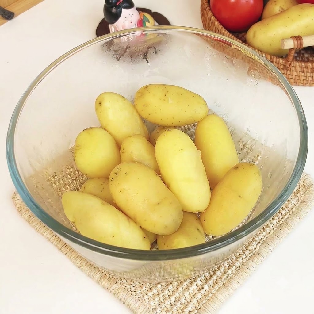 Patate cotte al vapore in una ciotola di vetro trasparente unite a burro e formaggio, schiacciate per ottenere un purè liscio.