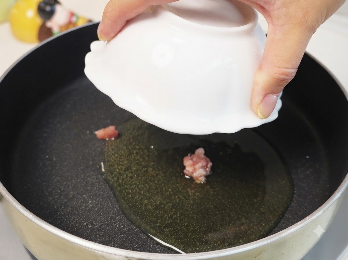 Carne di maiale macinata che cuoce in olio caldo allinterno di una padella nera a fuoco medio-basso.